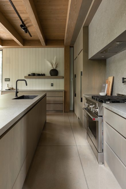 uisine contemporaine en bois et pierre, avec îlot en quartz gris, tabourets rembourrés et robinetterie noire mate, signée Ateliers Jacob.