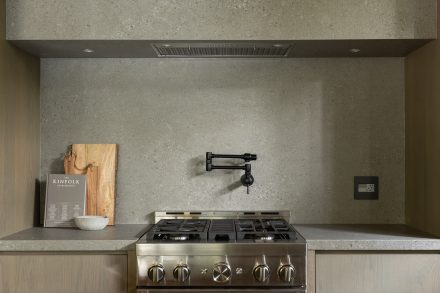 Détail d’une cuisine moderne avec surface en pierre grise, robinet noir mat, et livre Kinfolk en décoration sur fond de dosseret texturé.