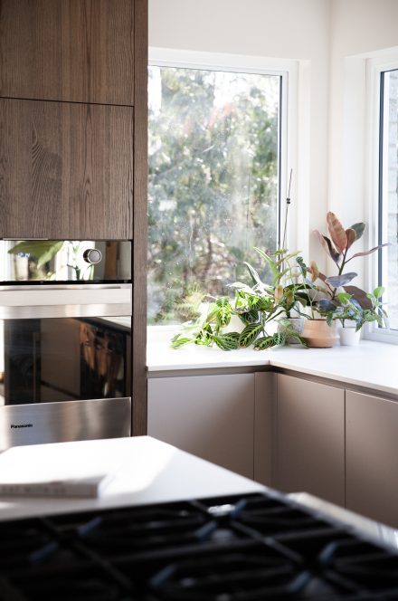 Détail d’un îlot en bois avec comptoir pâle et tabourets en cuir gris et noyer, baigné de lumière naturelle.