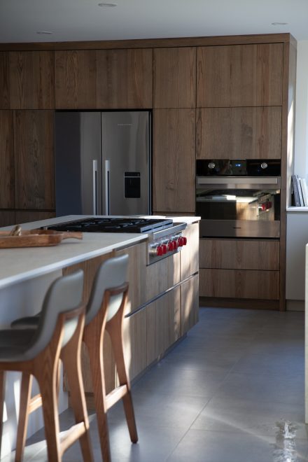 Cuisine minimaliste avec électroménagers encastrés, îlot central et grande fenêtre offrant une vue sur la cour.