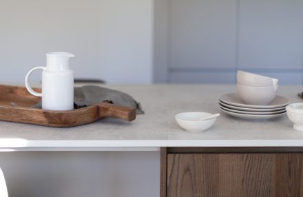 Détail d’un comptoir pâle avec vaisselle en céramique et plateau de service en bois, dans une cuisine épurée.