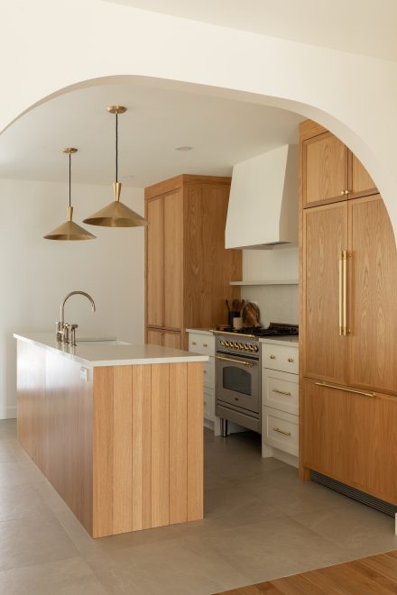 Cuisine contemporaine avec îlot en bois clair, luminaires dorés et électroménagers intégrés, conçue par Ateliers Jacob.