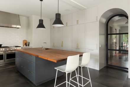 Cuisine contemporaine avec îlot marine et comptoir en noyer, armoires pleine hauteur et arches vitrées.
