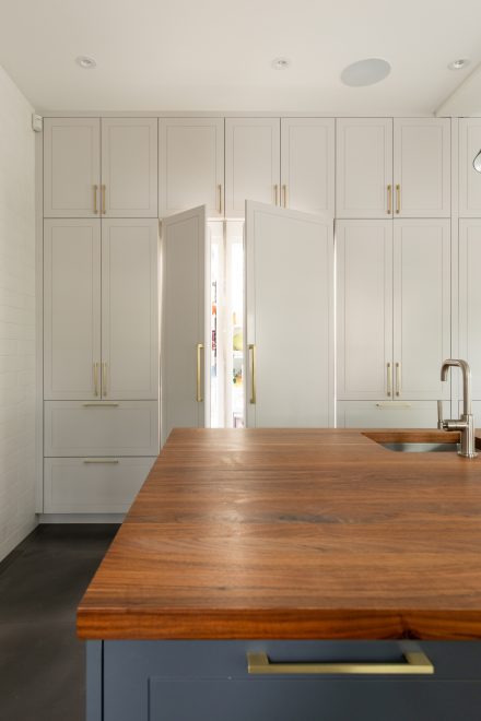  Détail des armoires pleine hauteur avec portes ouvertes sur un réfrégirateur dissimulé, dans une cuisine au style classique épuré.