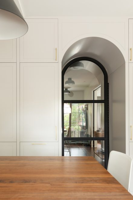 Porte vitrée arquée intégrée à un mur d’armoires sur mesure avec poignées dorées, liant cuisine et salle à manger dans une perspective élégante et architecturale.