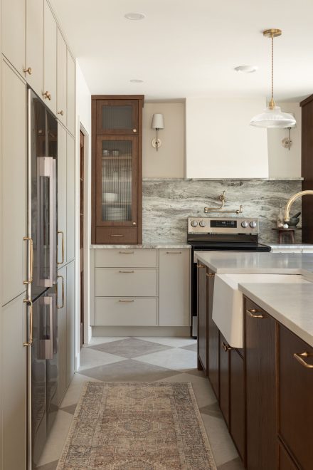 Cuisine de style classique et traditionnel conçue par Ateliers Jacob, avec armoires en bois et laque pâle, dosseret en pierre naturelle veinée, robinetterie dorée et évier de ferme blanc.