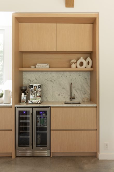 Coin café raffiné avec placage de bois clair, comptoir et dosseret en marbre, mini-cellier encastré et machine espresso professionnelle.