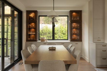 Vue traversante d’une cuisine haut de gamme avec îlot en bois foncé, tapis corridor, électroménagers professionnels et coin repas ouvert sur la terrasse.