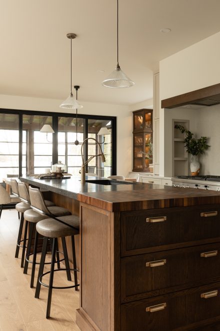 Vue latérale de l’îlot central avec tabourets élégants, tiroirs à poignées dorées et accès à une terrasse grâce à de grandes portes vitrées.