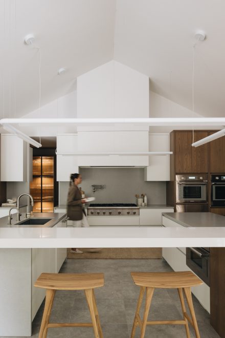 Cuisine contemporaine avec un grand îlot en cascade en pierre naturelle blanche, éclairage suspendu minimaliste, électroménagers intégrés et combinaison d’armoires en bois riche et blanc mat pour un contraste moderne et raffiné.