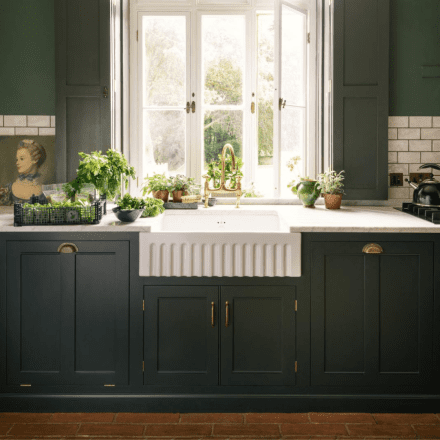 Cuisine au style classique avec un évier en céramique blanche et des plantes aromatiques disposées autour de la fenêtre.