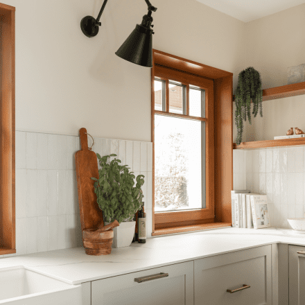 Cuisine moderne et minimaliste avec des plantes suspendues et des accessoires en cuivre, baignée de lumière naturelle.