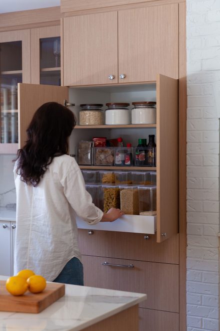 Femme accédant à un garde-manger bien organisé avec des contenants transparents et des bocaux en verre, intégrés dans une cuisine sur mesure en bois clair.