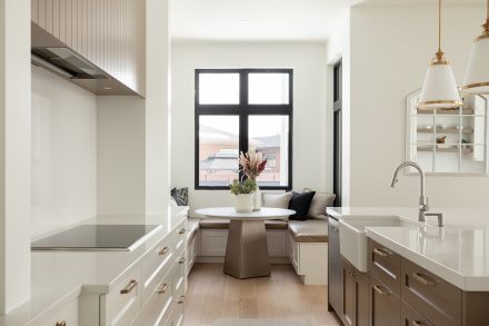 Une cuisine lumineuse et moderne avec des armoires blanches sur mesure, un îlot central en tons neutres et des accents dorés. 