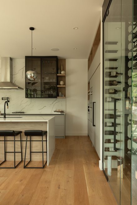 Cuisine contemporaine avec cellier vitré intégré, îlot central en quartz aux lignes épurées, et armoires murales minimalistes en bois clair et laque mate.