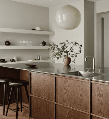 Cuisine minimaliste avec îlot en acier inoxydable brossé et armoires en bois foncé.