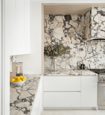 uisine lumineuse avec comptoirs, dosseret et hotte habillés de marbre Calacatta Viola, combinés à des armoires blanches minimalistes.