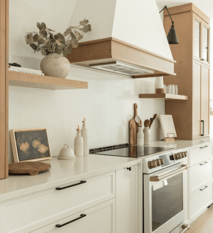 Cuisine farmhouse et chaleureuse avec comptoir en quartz Lynx de Sibérie, robinetterie dorée et hotte en bois blanc.