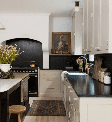 Cuisine au look traditionnel avec comptoirs en pierre ollaire (soapstone) noire et armoires crème à quincaillerie dorée.