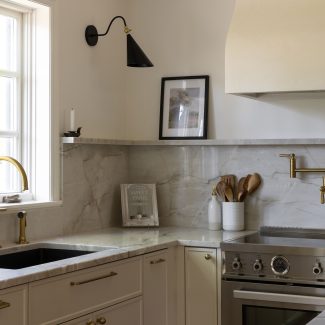 Cuisine élégante à Montréal avec comptoirs en marbre clair, robinetterie dorée, dosseret en pierre naturelle et cuisinière haut de gamme en acier inoxydable, conçue par Ateliers Jacob.