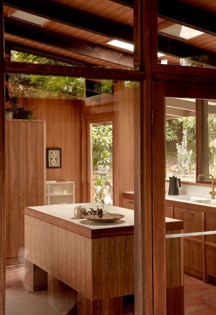 Cuisine rénovée dans une maison australienne des années 1960, avec îlot central en bois massif, plafond en lattes apparentes et fenestration généreuse.