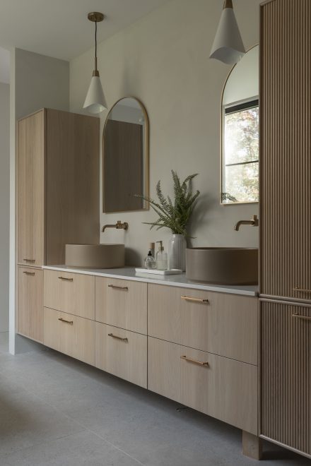 Salle de bain avec vanité Ateliers Jacob en chêne cannelé, double vasque ronde, robinetterie en laiton brossé et rangements fonctionnels.