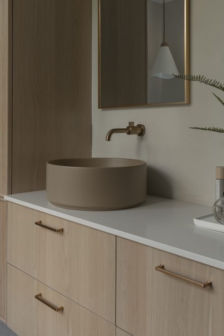 Vanité en chêne cannelé signée Ateliers Jacob avec vasque ronde posée, robinet mural en laiton brossé et comptoir en pierre naturelle.