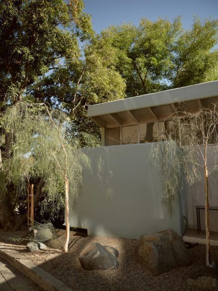 Façade extérieure de la Walker House conçue par R.M. Schindler, mettant en valeur l’esthétique Mid-Century moderne avec des lignes épurées, des arbres désertiques et un aménagement minéral.