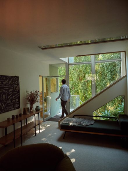 Intérieur lumineux de la Walker House avec de grandes fenêtres, mobilier minimaliste et vue sur la nature luxuriante, incarnant le style Mid-Century moderne.