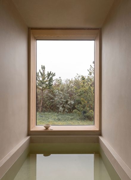 Bain encastré face à une grande fenêtre dans la salle de bain Heatherhill Beach House par Norm Architects, offrant une vue sur la nature pour un moment de détente.