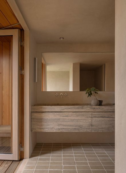 Salle de bain Heatherhill Beach House par Norm Architects avec vanité en pierre naturelle, lavabo encastré et miroir mural, mettant en valeur les teintes sobres et les matériaux nobles.