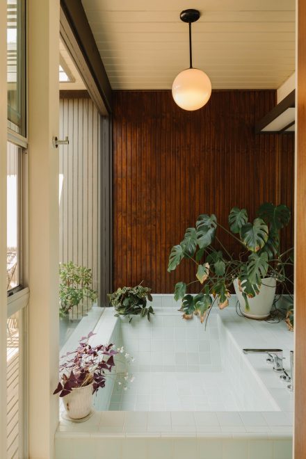 Salle de bain carrelée intégrée à une pièce vitrée, avec plantes d’intérieur et revêtement en bois sombre, dans une maison Mid-Century moderne.