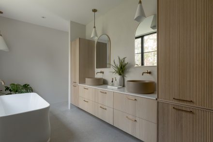 Salle de bain avec vanité Ateliers Jacob en chêne cannelé, double vasque ronde, robinetterie en laiton brossé et rangements fonctionnels.