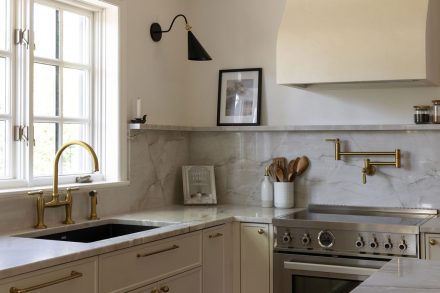 Cuisine haut de gamme conçue par Ateliers Jacob à Montréal, mariant des armoires crème avec des poignées en laiton, un îlot en bois clair et un comptoir en marbre. La hotte sculpturale et les luminaires suspendus ajoutent une touche artisanale et contemporaine à l’ensemble.