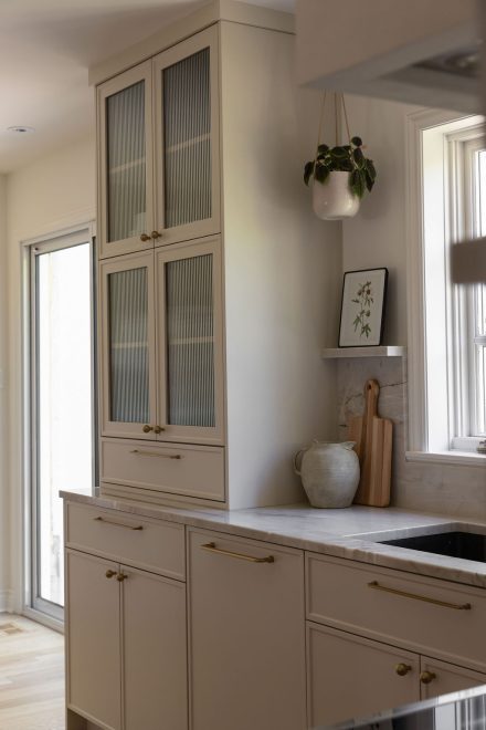 Cuisine haut de gamme conçue par Ateliers Jacob à Montréal, mariant des armoires crème avec des poignées en laiton, un îlot en bois clair et un comptoir en marbre. La hotte sculpturale et les luminaires suspendus ajoutent une touche artisanale et contemporaine à l’ensemble.