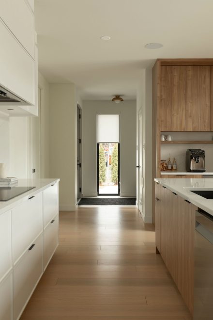 Cuisine moderne Ateliers Jacob avec comptoir en quartz blanc, grand îlot central en bois clair avec chaises noires, armoires pleine hauteur intégrées et robinetterie noire mate.