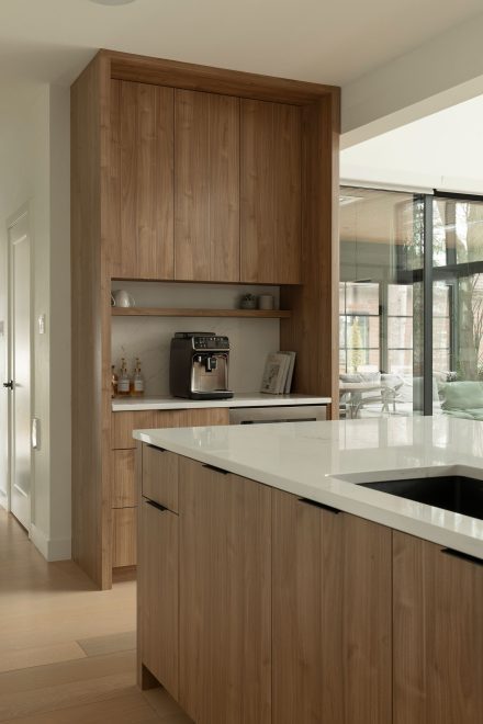 Coin barista intégré dans une cuisine Ateliers Jacob, avec armoires en bois naturel, étagère ouverte, comptoir en quartz blanc et machine à café encastrée.