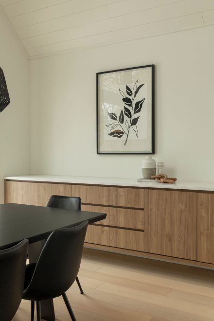 Desserte moderne sur mesure signée Ateliers Jacob, en bois naturel avec comptoir en quartz blanc, intégrée à la salle à manger design avec table noire et chaises en cuir.