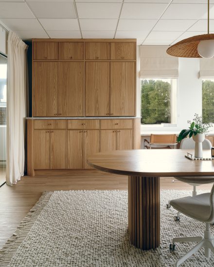 Vestibule des bureaux du média La Pièce, avec mur à lattes verticales en bois, banc en cannage, rangements intégrés, paniers tressés et plantes, dans une ambiance douce et lumineuse évoquant un hall d’entrée résidentiel.