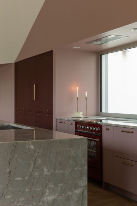 Cuisine sur mesure Ateliers Jacob avec îlot en pierre naturelle, armoires bourgogne mates, poignées en laiton 