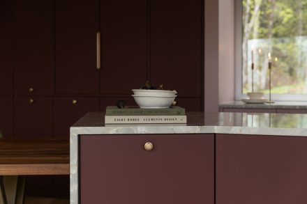 Aménagement de cuisine Ateliers Jacob avec armoires bourgogne sur mesure, électroménagers encastrés, comptoir en pierre naturelle et coin repas en bois massif