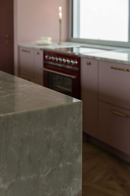 Détail de l’îlot de cuisine Ateliers Jacob avec comptoir en pierre naturelle aux veines minérales et armoires bourgogne sur mesure