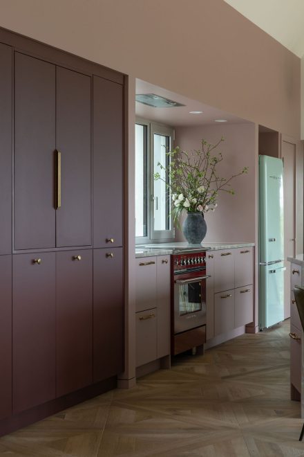 Cuisine sur mesure Ateliers Jacob avec îlot en pierre naturelle, armoires bourgogne mates, poignées en laiton avec réfrégirateur classic