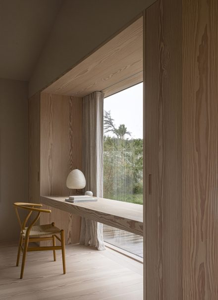 Face à la fenêtre, un bureau en bois est intégré au mur, éclairé par la lumière du jour et installé devant les arbres, dans cette maison signée Norm Architects.