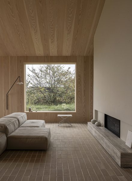 Depuis le salon, la nature entre par la fenêtre et s’installe dans la pièce, portée par la lumière changeante et la chaleur du bois.