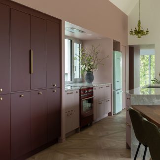 Cuisine sur mesure Ateliers Jacob avec îlot en pierre naturelle, armoires bourgogne mates, poignées en laiton