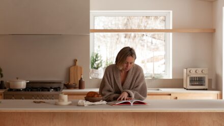 une femme dans sa cuisine Ateliers Jacob en train de regarder un livre de recette en papier