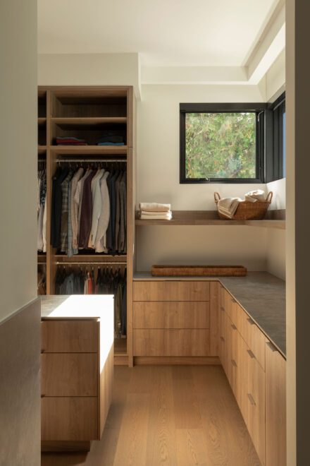 Walk-in sur mesure en bois avec garde-robe en angle, tiroirs intégrés et surfaces de pliage, conçu pour optimiser chaque espace