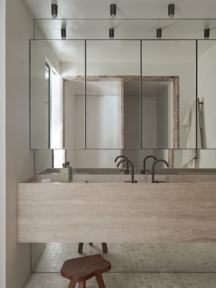 Un meuble-lavabo monolithique en travertin suspendu s’impose avec douceur devant un mur entièrement habillé de miroirs, amplifiant la profondeur et la lumière de la pièce. Projet: Madeleine Blanchfield Architects | Photo: Tom Ferguson