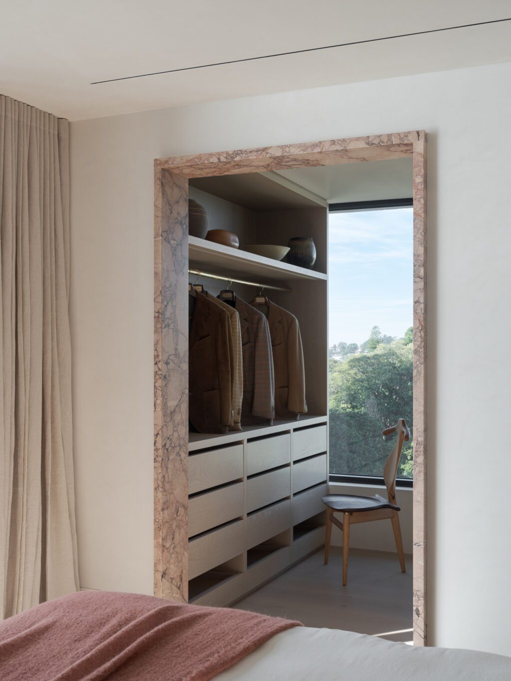 Walk-in sur mesure avec garde-robe intégré en bois clair, penderie ouverte et vue sur l’extérieur, aménagement fonctionnel et apaisant
